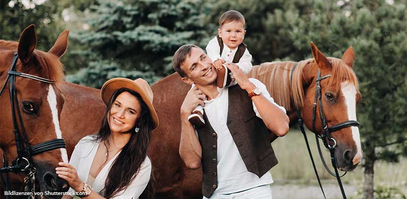 Junge Familie mit Sohn steht vor zwei Pferden und lächelt. Urlaub auf dem Reiterhof, ASS Altenburger