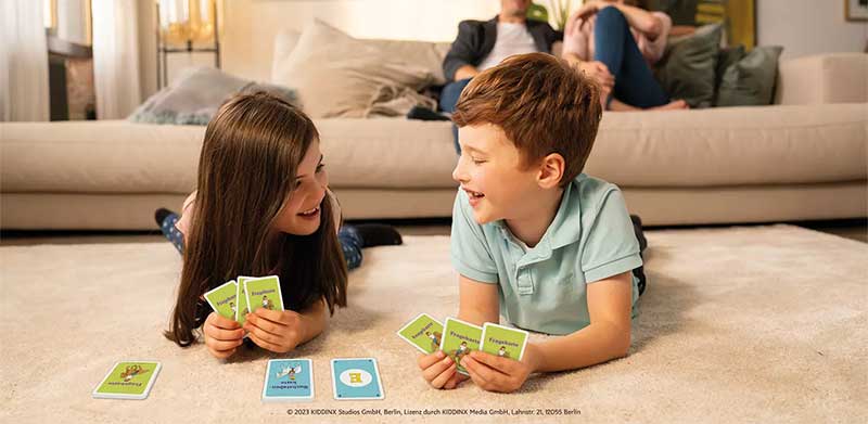 Junge und Mädchen liegen auf Wohnzimmer Boden und spielen Karten. Urlaub auf dem Reiterhof, ASS Altenburger