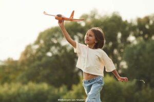 Mädchen mit braunen Haaren rennt durch Park und spielt mit Spielzeug Flugzeug. Spiele für draußen, ASS Altenburger