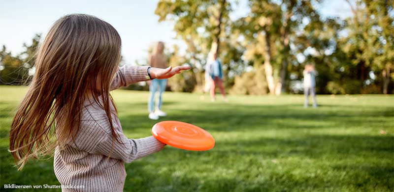 Mädchen wirft im Park eine Frisbee Scheibe zu ihrer Familie. Spiele für draußen, ASS Altenburger