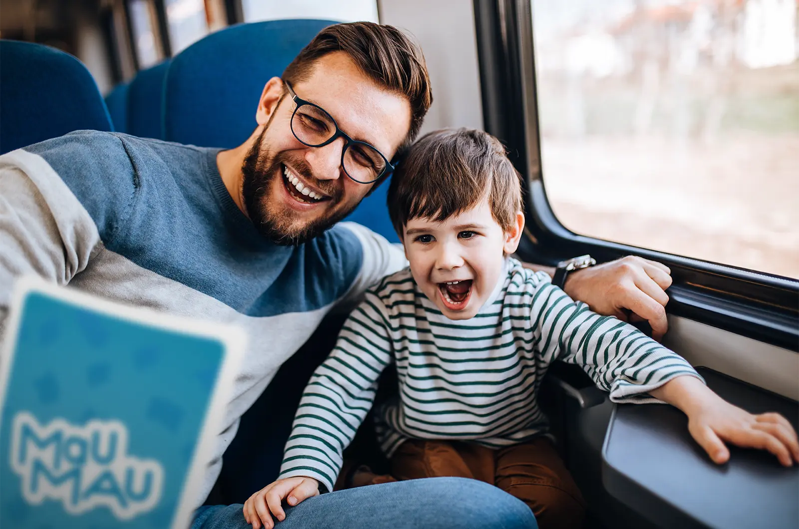 Vater und Sohn sitzen im Zug und schauen auf eine Mau Mau Karte. Reisespiele, ASS Altenburger