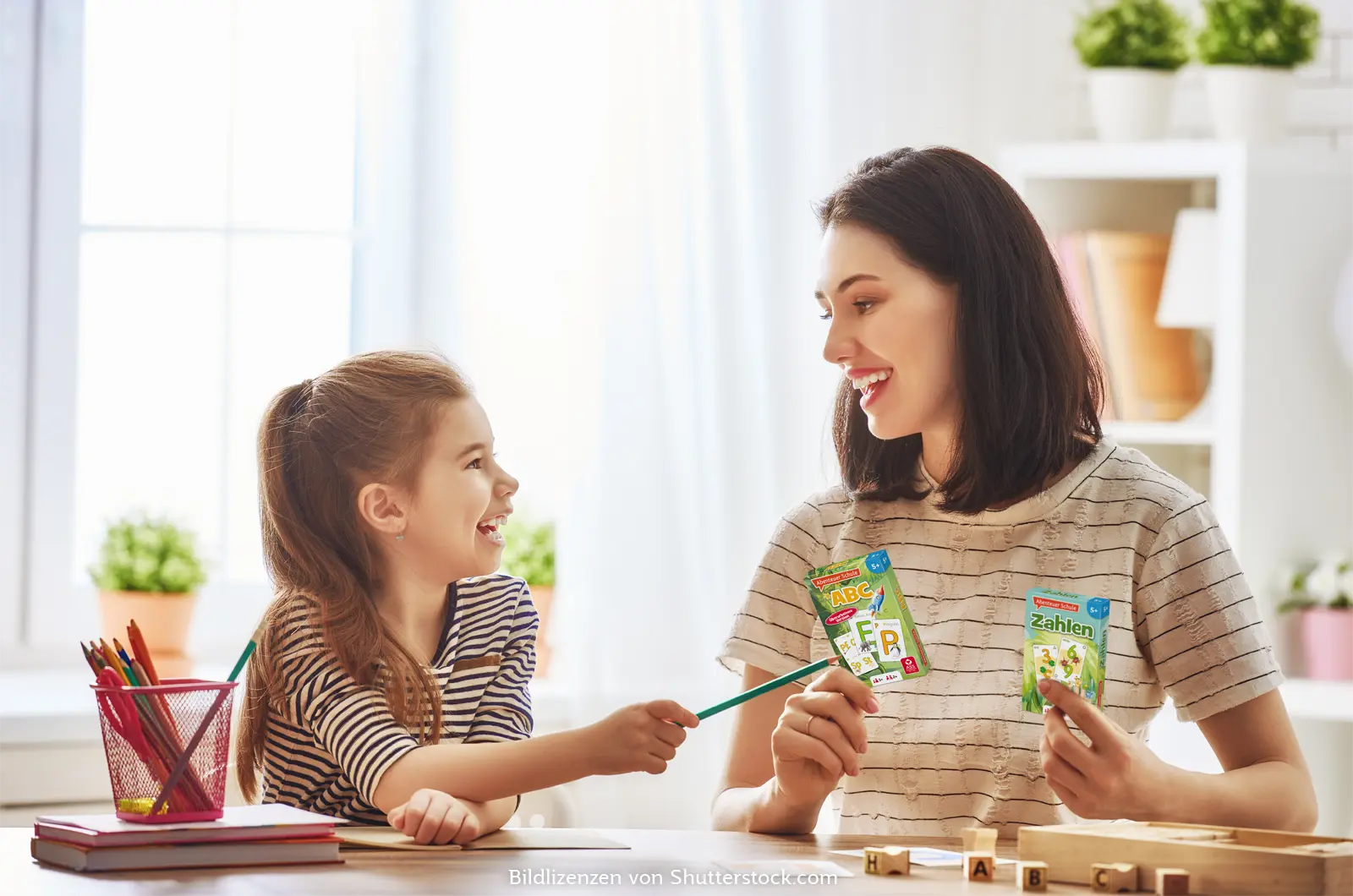 Mutter und Tochter sitzen am Tisch und lachen. Die Mutter hält zwei Kartenspiele in den Händen. Kinder Lernspiele, ASS Altenburger