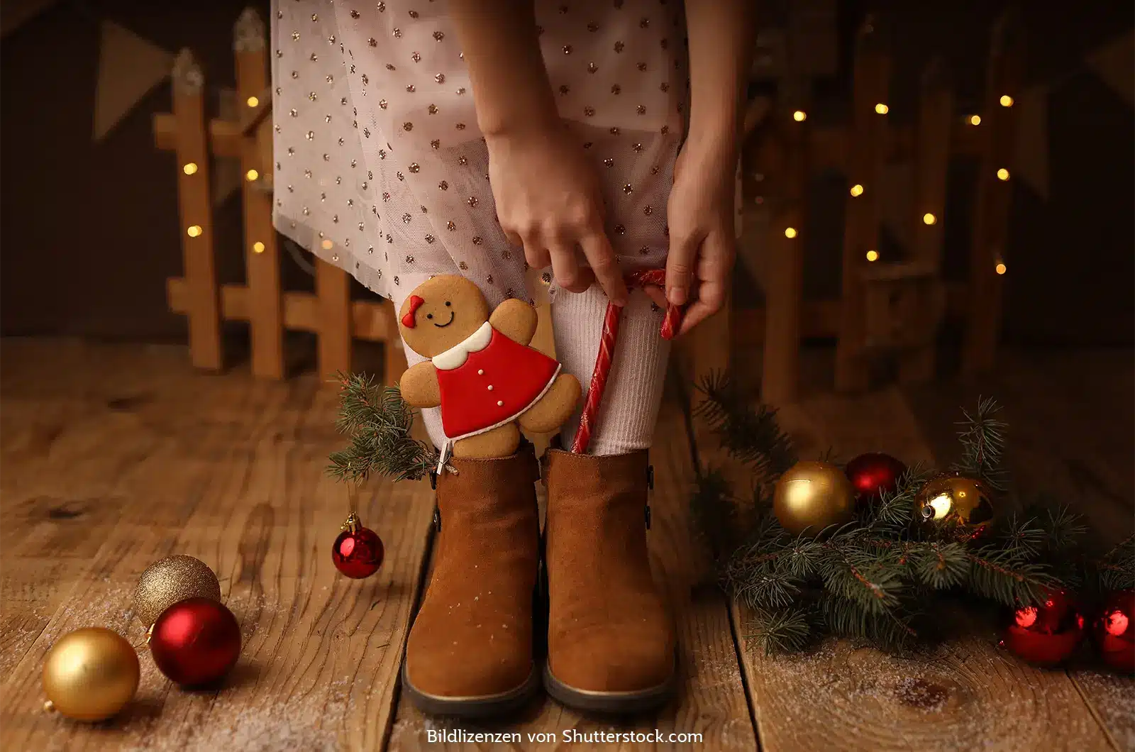 Beine und Füße eines Mädchens in braunen Stiefeln umringt von Weihnachtsdeko. Ein Lebkuchen und eine Zuckerstange stecken auch darin. Kleine Geschenke zu Weihnachten, ASS Altenburger